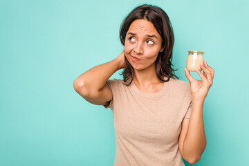 Young hispanic woman holding yogurt isolated on blue background touching back of head, thinking and making a choice.