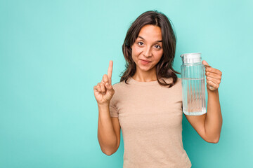 Young hispanic woman holding a water of jar isolated on blue background showing number one with finger.