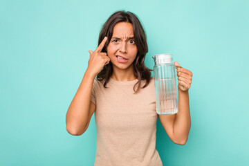 Young hispanic woman holding a water of jar isolated on blue background showing a disappointment gesture with forefinger.