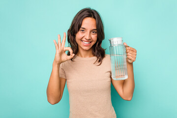 Young hispanic woman holding a water of jar isolated on blue background cheerful and confident showing ok gesture.