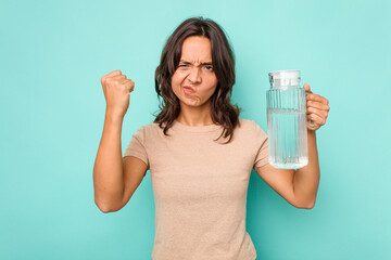 Young hispanic woman holding a water of jar isolated on blue background showing fist to camera, aggressive facial expression.