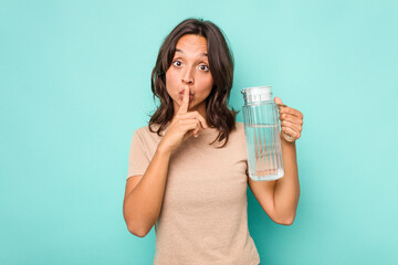 Young hispanic woman holding a water of jar isolated on blue background keeping a secret or asking for silence.