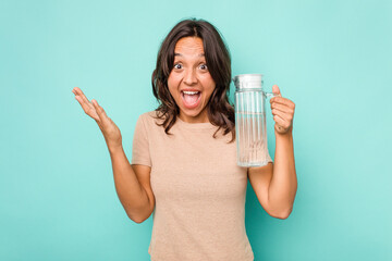 Young hispanic woman holding a water of jar isolated on blue background receiving a pleasant surprise, excited and raising hands.