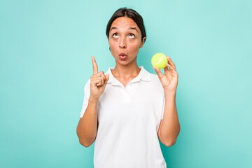 Young hispanic physiotherapy holding a tennis ball isolated on blue background pointing upside with opened mouth.