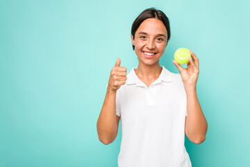 Young hispanic physiotherapy holding a tennis ball isolated on blue background smiling and raising thumb up