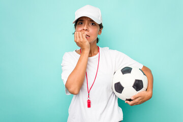 Young hispanic soccer referee woman isolated on blue background biting fingernails, nervous and...