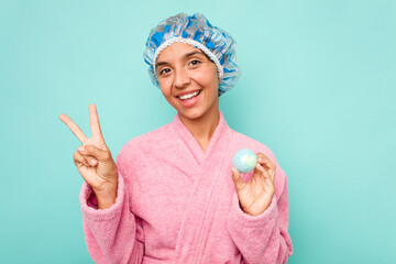 Young hispanic woman holding bathtub ball isolated on blue background joyful and carefree showing a peace symbol with fingers.