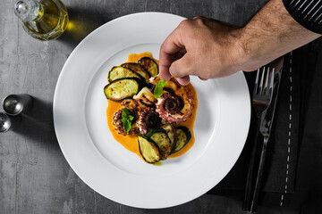 cooked octopus, served with courgettes and sauce serving on the table with cutlery. the hand of the chef