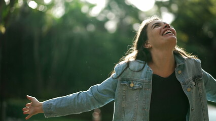 Carefree happy woman arms raised outside looking at sky feeling grateful. Person celebrating life standing in nature sunlight