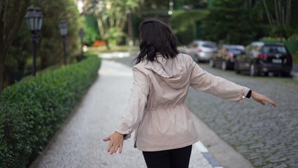 Back of carefree young woman jumping with joy in street flying in the air with arms raised pretending to fly