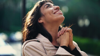 A grateful hispanic woman praying to God with hands clenched looking at sky smiling. Spiritual...