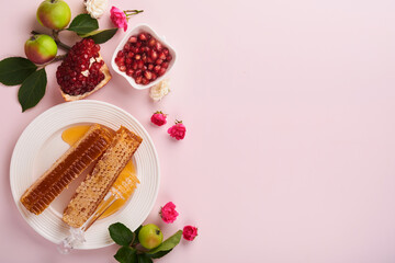 Rosh Hashanah. Honey jar, honeycomb, apple and pomegranate on simple pink background. Jewish New...