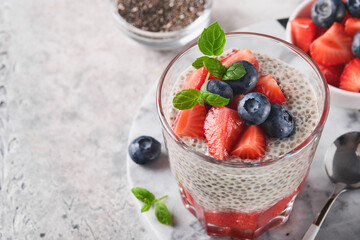 Chia strawberry pudding. Healthy vegan breakfast chia seeds pudding with fresh berries and mint in glass on gray concrete background. Concept of healthy eating, dieting, fitness menu. Selective focus.