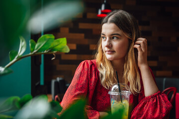 Attractive young woman in a red dress in a cafe with lemonade.