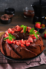 Dark Chocolate Bundt Cake with Ganache Icing and strawberry on dark stone or concrete table background. Festive cake. Selective focus
