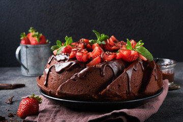 Dark Chocolate Bundt Cake with Ganache Icing and strawberry on dark stone or concrete table background. Festive cake. Selective focus
