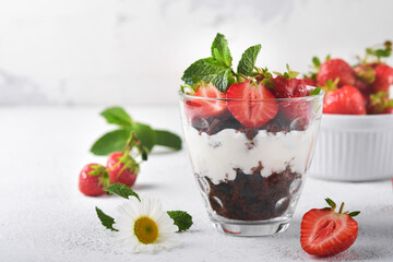 Trifles. Brownies, fresh strawberry and mascarpone cream servered in layers on glass on white background. Portion desserts. No baked brownie cheesecake with fresh berries in a glass.