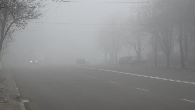 Cars in the road in city in fog. Bad winter weather and dangerous automobile traffic on the road. Light vehicles in foggy day