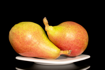 Two organic juicy pears in a white ceramic plate, close-up, isolated on a black background.