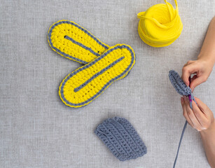 Women's hands crochet. On the table is club of yellow knitted yarn, finished products. View from above. Selective focus. Images for websites about knitting, hobbies