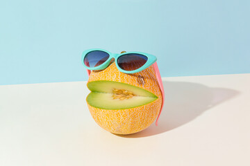 Abstract creative summer fruit scene made of cut melon with sunglasses on isolated pastel blue and...