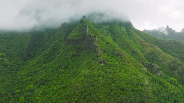 Cinematic scenery tropical rainforest climate during global warming. Aerial shot flying in the clouds covering green mountain peaks on Na Pali coast National park, in Kauai island, Hawaii state, USA