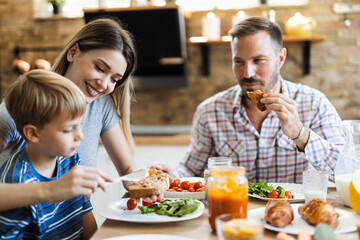 Young mother feeding her small boy while having breakfast in the kitchen