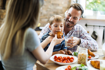 Young happy parents feeding their son during breakfast time in the kitchen