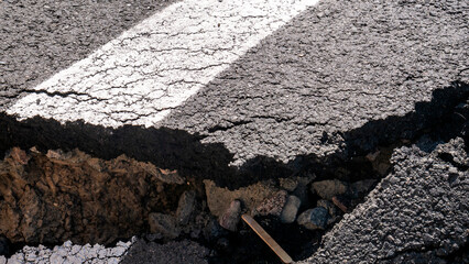 Dangerous stretch of road with damaged asphalt. The accident site is fenced off with black and...