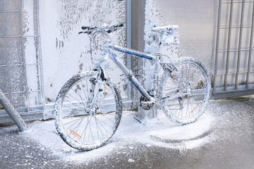 Plakat Washing a bicycle with a foam jet at a car wash. The bike is covered with foam. Self-service. Bicycle maintenance.
