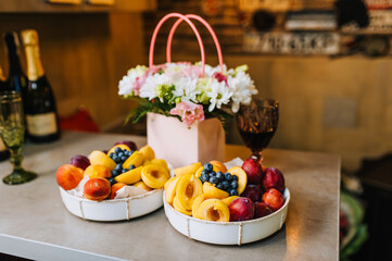 A basket of flowers and fresh fruit with a glass of champagne are on the table as a birthday present. Festive photo.