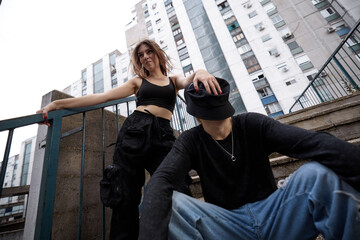A teenage girl is joking with her friend and putting a hat on his face while standing in an urban...
