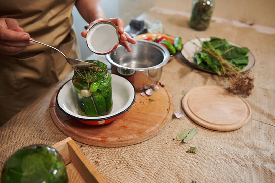 Close-up Of A Housewife Pouring Brine Or Marinade Into A Glass Jar While Marinating Cucumbers In The Home Kitchen. Canning. Pickling. Harvest Conservation For Winter. Preserving Seasonal Vegetables