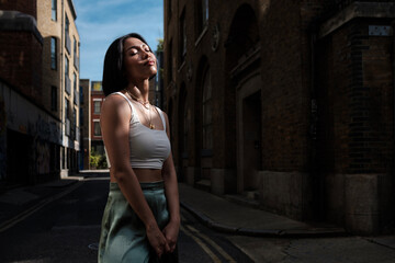 A young asian female is standing in a narrow London street enjoying the morning sun.
