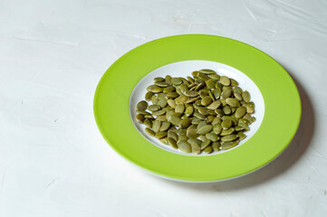 pumpkin seeds on a plate with a green border on a gray background, copy space.