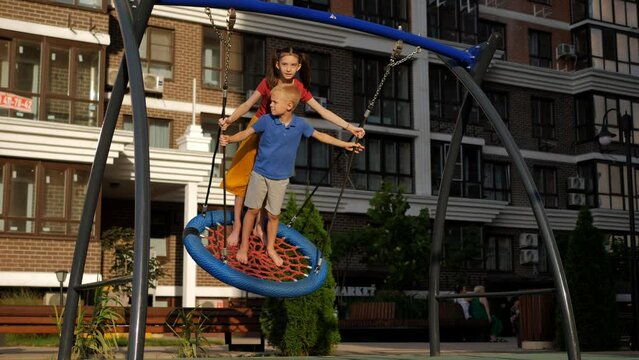Happy children swing on a round swing on the playground in the courtyard of a residential area.