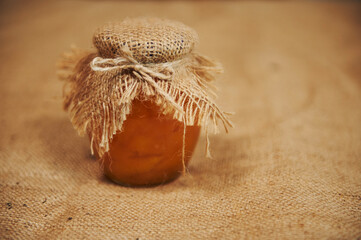 Still life. Jar of homemade peach jam with a burlap on the lid, on the table with linen tablecloth....