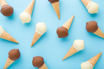Waffle cones of white vanilla and black chocolate ice cream on light blue table background. Pastel...