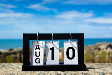 Aug 10 calendar date text on wooden frame with blurred background of ocean.