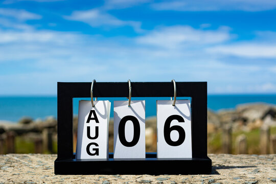 Aug 06 calendar date text on wooden frame with blurred background of ocean.