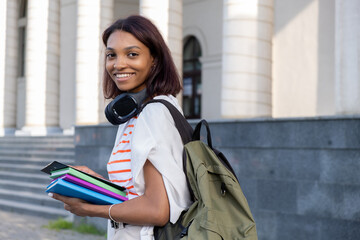Portrait of a young college girl holding folders and notebooks and walking down the street to go to school or college. Student girl smiling and happy