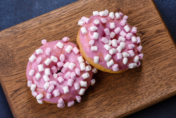 Pink glazed doughnut and marshmallow with Christmas decorations on a wooden cutting board