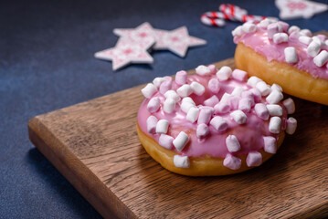 Obraz na płótnie Canvas Pink glazed doughnut and marshmallow with Christmas decorations on a wooden cutting board