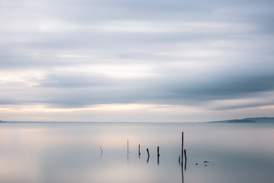 Long exposure view of fishing net poles on a lake, with perfectly still water and moving clouds