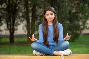 Meditating keeping mudra gesture. Upset teen girl meditating sitting outdoors, meditating - obrazy, fototapety, plakaty