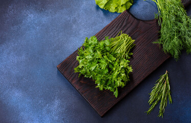 Salad, parsley and dill on a dark cutting board against a blue concrete background