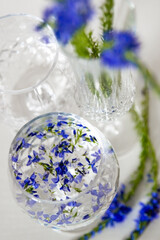 Beautiful crystal glasses, with water and blue flowers, on a white background. White background, crystal glasses filled with water and blue flowers.