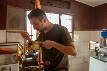 Male q grader holding a spoonful of coffee while tasting while standing near coffee machines at the factory
