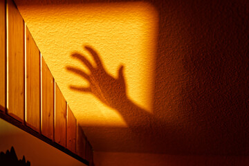 silhouette of aggressive monster hand and casting shadows on the orange wall at golden hour making...