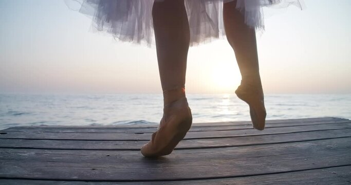 Legs of ballerina in pointies and tutu dancing on tiptoes in sunrays on wooden pier. Unrecognizable talented confident Caucasian woman performing at dawn outdoors. Cinema 4k ProRes HQ
